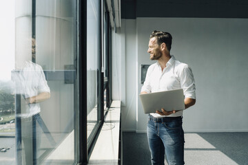Mature businessman using laptop at the window in empty office