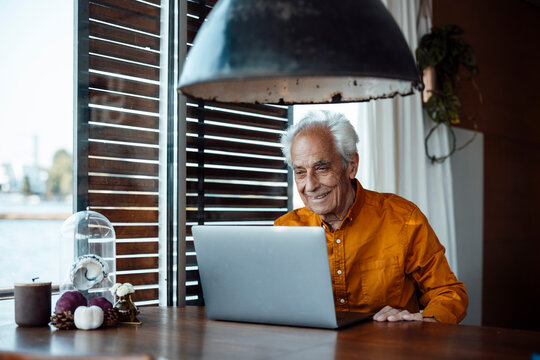 Smiling senior man with laptop sitting at table in houseboat