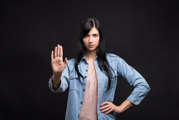 Attractive caucasian brunette girl in shirt showing hand and palm stop gesture isolated on black...