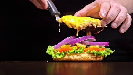Craft burger is cooking on black background. Consist: sauce, lettuce, tomato, red onion, pickle, cheese, bacon, air bun and marbled meat beef. Not made ideal. Looks real, loving hand made.