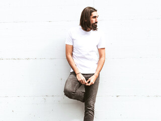 long-haired and bearded man posing against a white wall waiting for