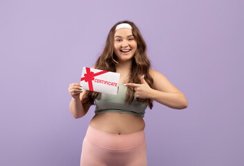 Glad smiling excited plus size european millennial female in sportswear pointing finger at certificate