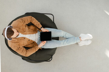 Top View Of Man Using Tablet Wearing Headphones Sitting Indoors