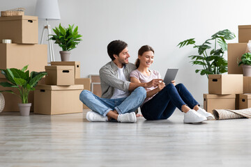 Fototapeta na wymiar Cheerful young caucasian man and woman in casual enjoy moving, sitting on floor among cardboard boxes with belongings
