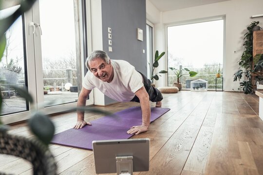 Smiling Senior Man Doing Push-ups On Exercise Mat At Home