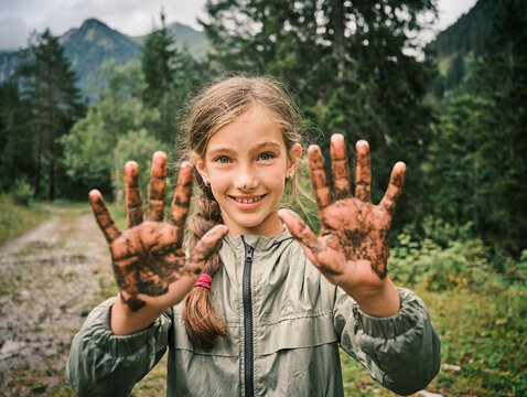 Smiling girl showing muddy hands in forest