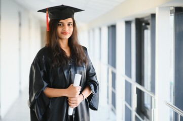 Happy Indian university student in graduation gown and cap holding diploma certificate.