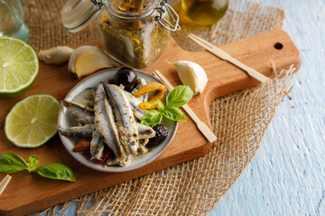 Mediterranean appetizer, anchovy fish in olive oil and herbs in a small bowl. Top down view.