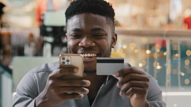 Young happy smiling guy shopper client online store customer makes purchase paying by credit card using instant mobile payments using smartphone buying distantly E-banking app service safe payment