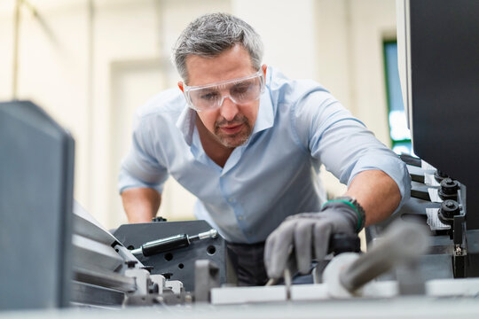 Businessman wearing protective eyewear examining machinery in factory