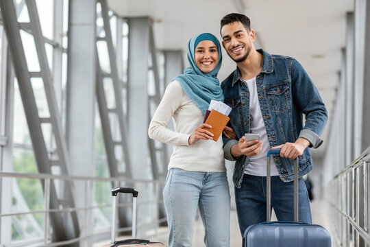 Portrait Of Happy Islamic Couple Standing At Airport With Luggage And Smartphone