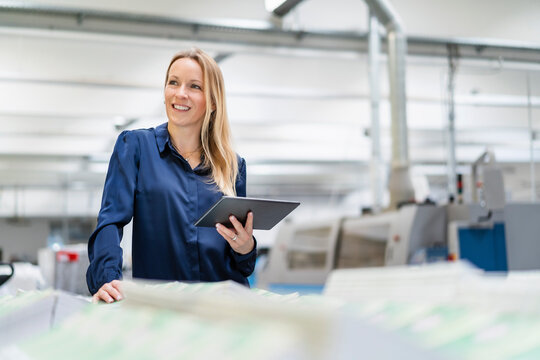 Smiling blond businesswoman with tablet PC in factory