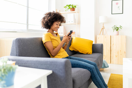 Happy woman text messaging through mobile phone on sofa at home