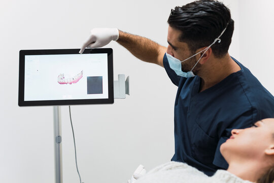 Dentist showing teeth X-ray to patient over intraoral scanner screen in clinic