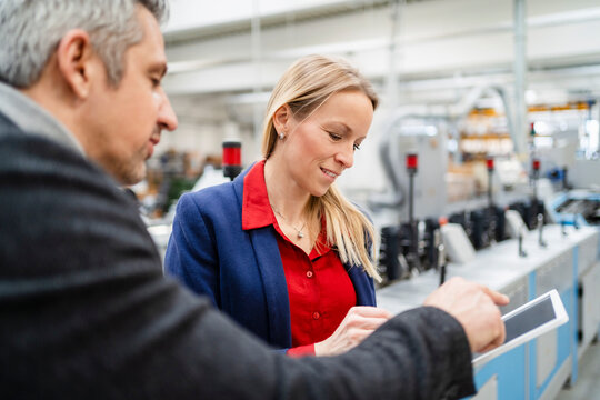 Businessman discussing over tablet PC with blond businesswoman in factory
