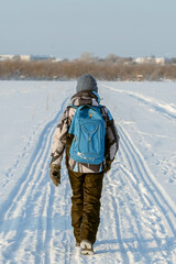 A boy walks along the road in winter with a backpack through a snowy wasteland. The concept of the road to school in the village, travel in winter.