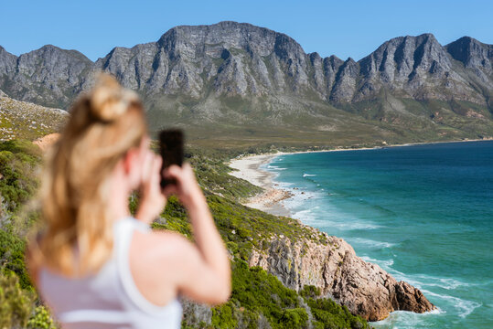 Young woman photographing mountains through smart phone on sunny day
