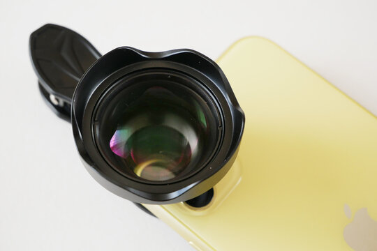 yellow smartphone with external lens on clip on white. An additional portrait lens and clip are supplied with the mobile phone
