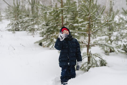 Happy boy wearing warm clothing standing in snow forest by tree