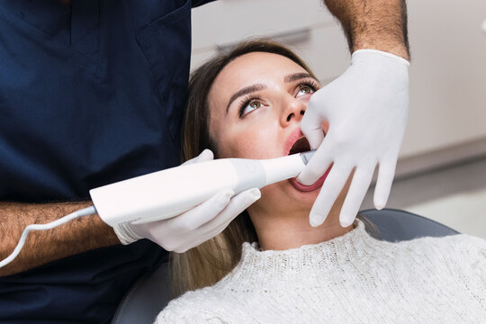 Dentist with intraoral scanner examining patient's teeth at clinic