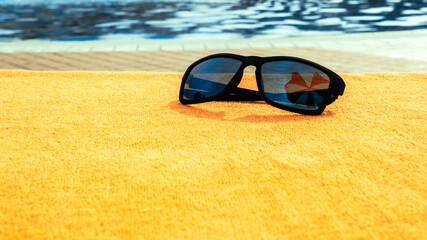 Sunglasses pool summer background. Beach pool equipment with travel sunglasses on yellow holiday towel. Sun glasses near swimming pool, holiday concept.