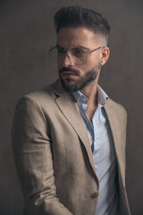 bearded young fashion man with glasses in beige suit looking to side