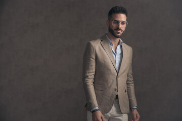 confident bearded man with eyeglasses in beige suit looking away