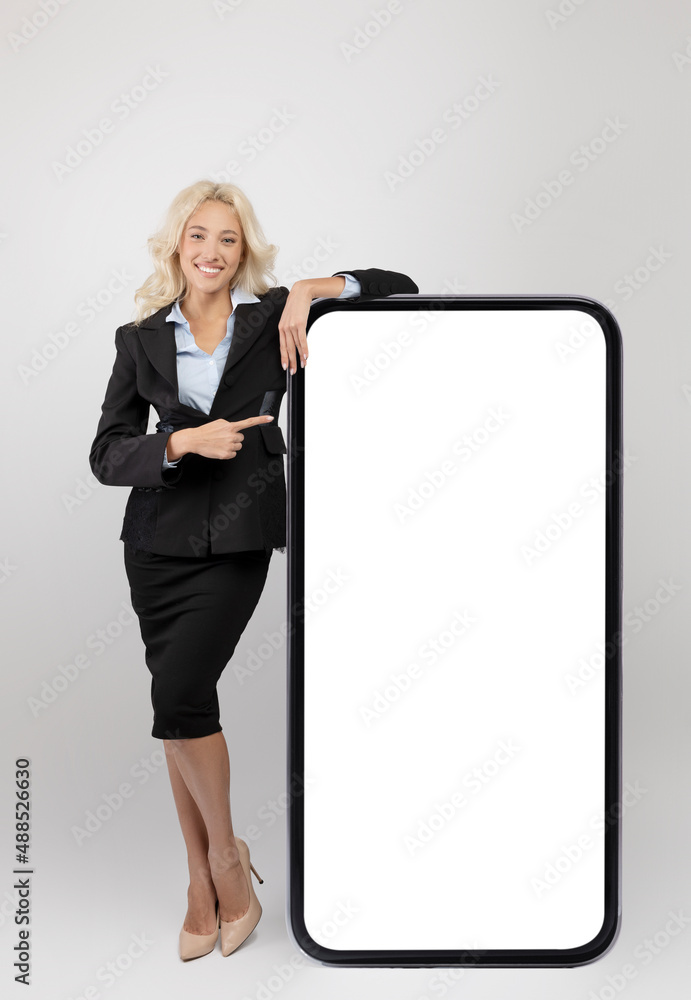 Canvas Prints Young happy businesswoman leaning on giant smartphone with empty white screen and pointing at big device, mockup