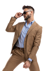 attractive young guy in brown suit looking to side and adjusting sunglasses