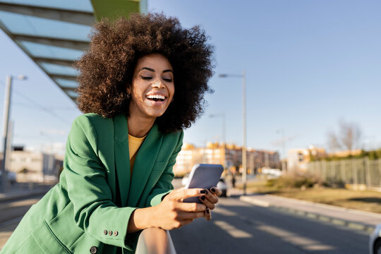 Cheerful commuter using smart phone leaning on railing