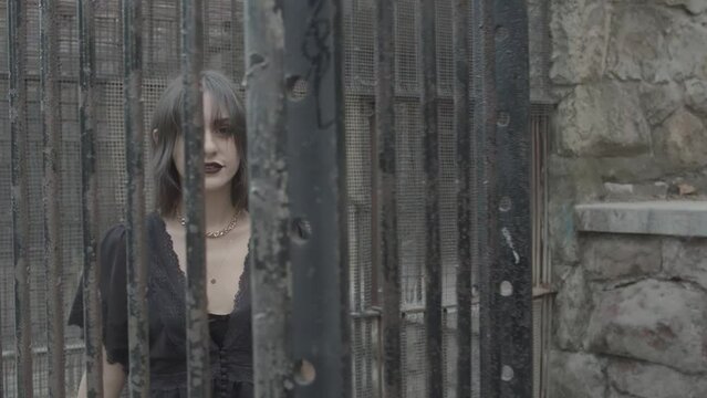 Slow motion shot of a goth girl behind rusted animal cage bars