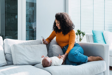 Mother using smart phone sitting by baby boy on sofa at home