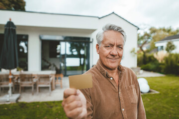 Smiling senior man showing credit card at backyard