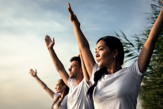 Group of people doing yoga exercises by the lake at sunset.