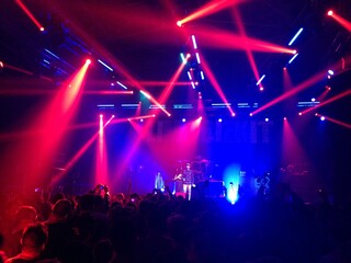 Laser show at live performance. A bunch of music fans in front of a stage. Red lights above the...