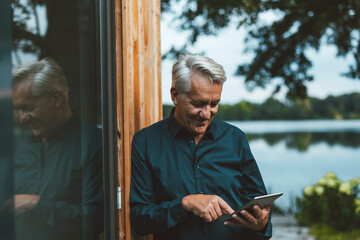 Smiling senior man using tablet PC by glass wall at backyard