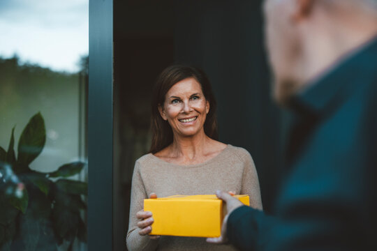 Happy woman receiving package from delivery person at doorway