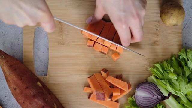Woman cutting sweet potato into cubes on a wooden board