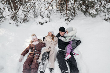 dad and mom and daughters lying in the snow in the winter forest. High quality photo