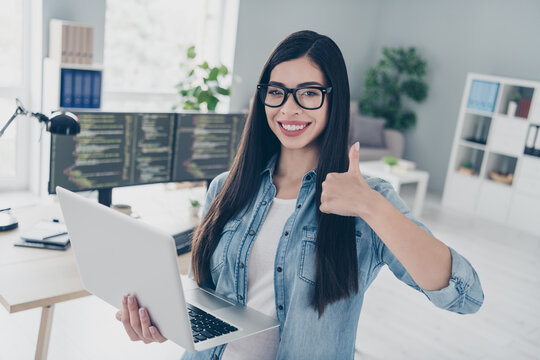Portrait of attractive cheery successful intellectual girl expert web designer using laptop showing thumbup at workplace workstation indoors