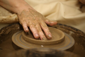 A potter makes a product out of clay, on a potter's wheel. Women's hands.
