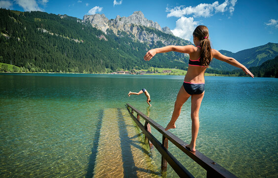 Girl with arms outstretched balancing on railing amidst lake