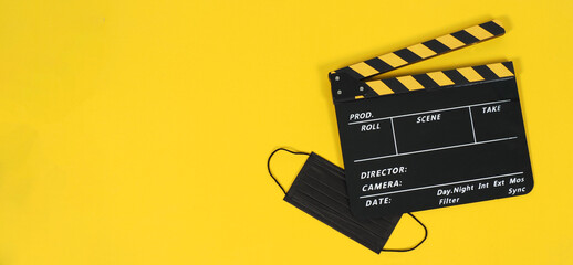 Black clapper board and black face mask on yellow background.