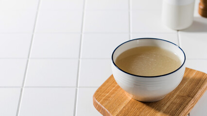 Homemade bone broth in a white bowl on a wooden board. The concept of a healthy diet. Copy space.