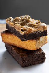 Stack of delicious dessert slices. Brownie, macadamia almond and chocolate caramel bar. Close up vertical orientation.