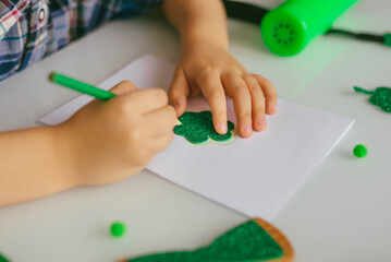 One toddler boy makes a postcard for the Patrick's Day holiday. Traditions, technologies, holidays concept.