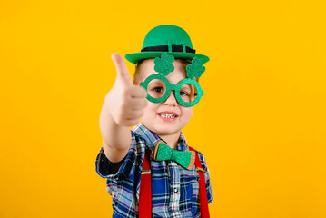 Funny toddler boy with green glasses and a hat on a yellow background. Happy Patrick's Day.