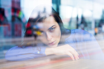 Close up face of young stylish woman. Thoughtful concept. Woman at a cafe while gazing through the window glass. Beautiful girl in the window watching, close up.