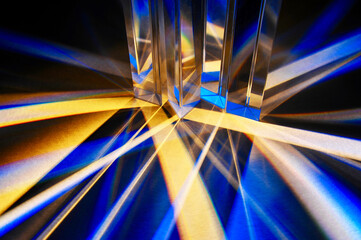 Closeup of group of reflective triangular glass prisms dispersing and spreading beam of light in to spectrum and criss cross line on white paper background. Refracted blue light with artistic pattern