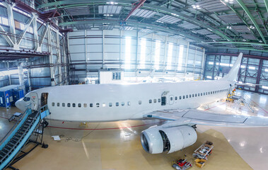 White passenger airliner in the hangar. Airplane under maintenance. Checking mechanical systems for...